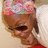 Pixelated image of a person with brown hair wearing a red top and pink floral headpiece against light background.