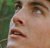 Pixelated close-up of a person's face showing eyes, nose, and mouth against green foliage background.