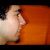 Pixelated profile view of a person with light skin tone against an orange background, showing partial facial features and dark hair.