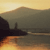 Pixelated landscape with dark silhouette of structures against a gradient sky transitioning from yellow to gray, reflecting in water below.