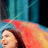 A woman with long dark hair and a red-orange headscarf smiles against a blue curtain background, her face turning slightly left to right across frames.
