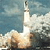 A rocket launches with smoke and fire against a blue sky background.