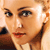 A pixelated close-up of a person's face with light skin tone, dark eyebrows, and red lips, showing partial facial features and a blurred background.