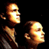 Pixelated static image of two humanoid figures with glowing faces against a black background, rendered in warm tones and low resolution.