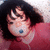 A person with dark hair and a red top lies on a light surface, mouth open with a blue object inside, eyes closed in a static pose.