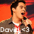 A person in a brown jacket and red tie holds a microphone against an orange background with text "David <3" visible.