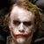 A pixelated close-up of a person with white face paint, dark eye makeup, and a red smile, set against a dark background with green and gray sections.