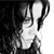 Black-and-white pixelated image of a figure with long hair, wearing a light-colored top, holding a dark object near the face.