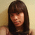 Pixelated portrait of a person with long dark hair and bangs against a light brown background.
