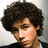 Pixelated image of a person with curly brown hair and a dark jacket over a light shirt, with text overlays on a black background.