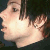Pixelated close-up of a person's face showing light skin, dark hair, and a neutral expression against a dark background.