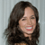 A static pixelated image of a person with long dark hair, smiling with visible teeth, against a light gray striped background.