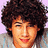 A person with curly brown hair and light skin wears a gray shirt with blue stripes against a light purple background.