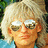 Pixelated close-up of a person with light-colored hair and glasses, wearing a blue garment against a blurred background.