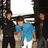 Three pixelated figures stand in a row; the central figure wears blue shirt and light pants, flanked by two dark-clad figures with obscured faces.