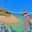 Pixelated beach scene with a person standing in shallow water, wearing sunglasses and a light-colored shirt, against a blue sky and turquoise sea.