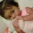 A pixelated image of a person with dark hair wearing a white top and pink sleeves, holding an object near their face.