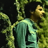 Pixelated image of a person with brown hair wearing a light green shirt, standing against dark background with blurred foliage.