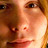 Pixelated close-up of a human face with warm brown and orange tones, showing eyes, nose, mouth, and partial hair against a blurred background.