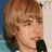 Two side-by-side pixelated images of a person with light brown hair holding microphones, one showing the mouth open and the other with fingers near the lips, below which is yellow text on black background.