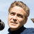 Pixelated close-up of a person with light brown hair wearing a dark turtleneck against a light blue background with partial shapes on the sides.