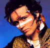 A mirrored image of a person with dark curly hair, white face paint stripes, and large earrings against a blue background.