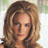 Pixelated close-up of a person with light brown hair styled in loose waves, wearing dark clothing against a blurred background.