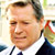 Static pixelated image of a person in formal attire with visible facial features and partial background elements.