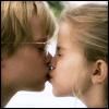 Static close-up of two people kissing with visible facial features and light-colored hair against a bright background.