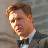 Pixelated static image of a man in formal attire with brown hair and light skin, cropped to show upper torso against gray background.
