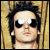 Pixelated static image of a person with dark hair, sunglasses, and light skin against a yellowish background.