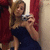 A woman in a dark blue strapless dress takes a mirror selfie with a silver digital camera, standing against red and white striped fabric.
