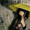 A person in a black-and-white striped shirt holds a yellow umbrella over their head, with a blurred background of newspaper pages.
