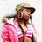 Pixelated image of a person with long dark hair wearing a light green cap and pink outfit, holding an object near their face.