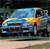 Pixelated blue car with yellow and orange highlights on a dark background, viewed from a low angle with visible wheels and a simplified front grille.
