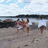 Pixelated beach scene with four figures on sand, water and sky in background.