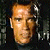 Pixelated close-up of a person's face with light brown hair, neutral expression, and dark background with faint white shapes.