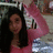 A person with long dark hair wears a pink top, holding a pink object with black text against a blurred background.