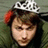 Pixelated image of a person with a silver tiara, red hair, and green clothing, with text overlays on a black background.