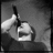 Black-and-white pixelated image of a figure holding an object near their face, with visible hand and partial facial features.