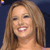 A pixelated close-up of a person with long light brown hair smiling, showing teeth, against a dark blue background.