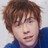 Pixelated close-up of a person with brown hair and blue clothing against light background.