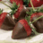 Pixelated image of chocolate-covered strawberries with green leaves on a white surface, alongside repeated pink text on brown and gray backgrounds.