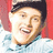 A pixelated image shows a person in a light blue shirt and dark cap against a red background, with pink text on the right side.