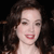 A pixelated close-up of a person with dark curly hair, light skin, and red lips against a black background.