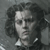 Pixelated grayscale portrait of a person with curly hair, wearing a dark jacket and white shirt, against a gray background.