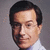 A pixelated portrait of a man with dark hair and glasses, wearing a light-colored collared shirt against a gray background.