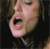 Pixelated close-up of a person's face showing mouth open in a shout or yell, dark background, visible teeth, and closed eyes.