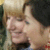 Static image of two people in close physical proximity with one person's hand near the other's face, set against a blurred background.