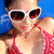 A person in a red polka-dot swimsuit and white sunglasses poses against a blue background with subtle wave patterns.